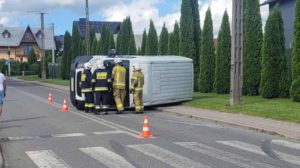 Biały bus leży przewrócony na bok, obok strażący
