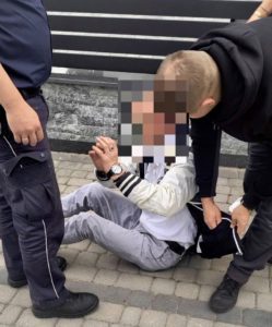 Dwaj policjanci stoją obok skutego mężczyzny siedzącego na chodniku