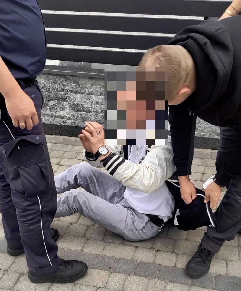 Dwaj policjanci stoją obok skutego mężczyzny siedzącego na chodniku
