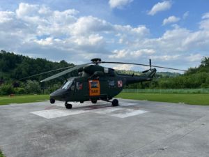 Śmigłowiec stoi na płycie lotniska, na tle gór i niebieskiego nieba