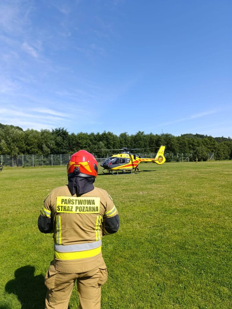 Strażak na pierwszym planie, w tle śmigłowiec ratowniczy