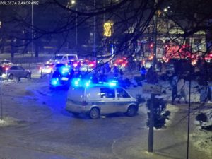 noc, samochody służb z włączonymi światłami, tłum ludzie przed sklepem