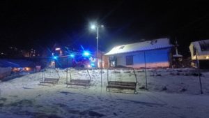 Nocna akcja straży pożarnej w Szczawnicy, przykryte śniegiem krzesełka wyciągu narciarskiego i domy w tle.