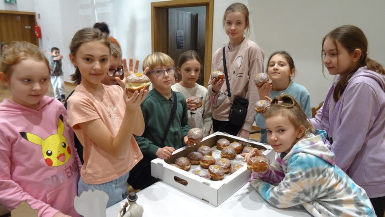 Grupa dzieci jedząca pączki, na stole pudełko z pączkami