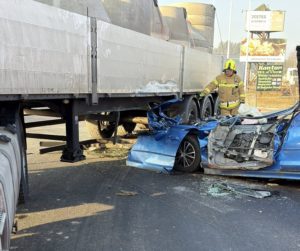 Zniszczony samochód osobowy po zderzeniu z ciężarówką na drodze krajowej nr 7 w miejscowości Chyżne. Na miejscu wypadku pracuje strażak, a pojazd osobowy jest poważnie zmiażdżony pod naczepą ciężarówki.