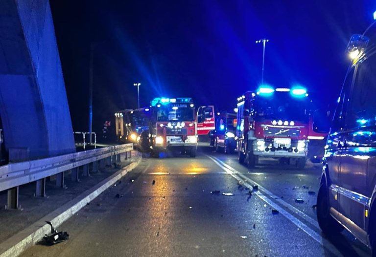 Wozy strażackie na włączonych światłach stoją przy moście w Kąclowej, na drodze widoczne są rozbite części samochodu po nocnym wypadku.