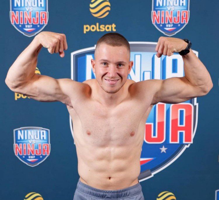 Młody chłopak prezentuje muskuły na tle ścianki reklamowej